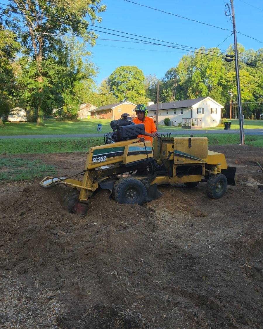 Crew member in a helmet operating a stump grinder in a front yard